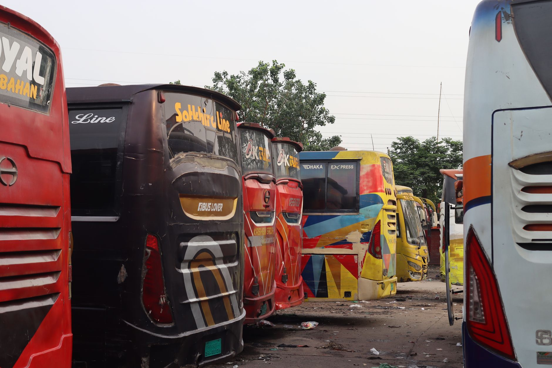 Row of colorful buses parked outdoors in an urban lot with a clear sky.